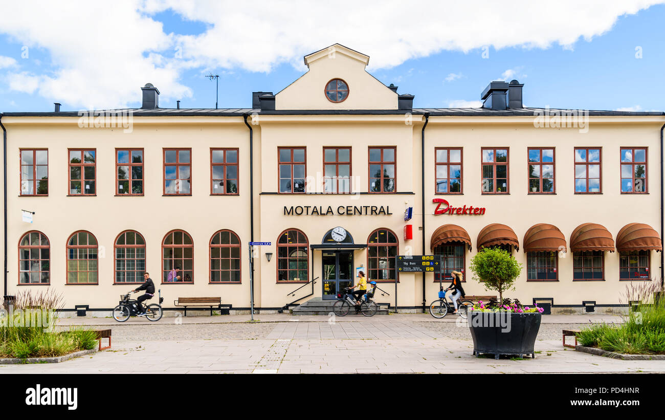 Motala, Sweden - June 30, 2018: Ordinary summer day with three people bicycling past the railway station and travel center building. Stock Photo