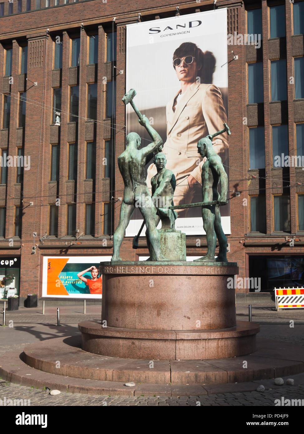 Opposing lifestyles in the centre of Helsinki Finland, sculpture of industrial ironworkers in bronze set against a gigant board promoting Sand brand Stock Photo