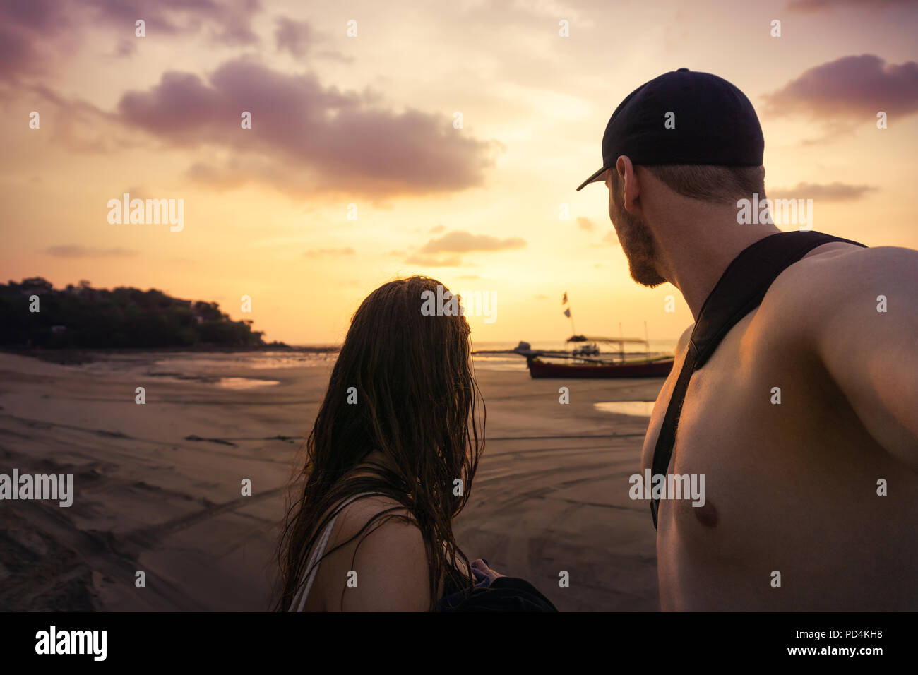 A couple stand on the beach of thailand looking at the golden purple sunset Stock Photo