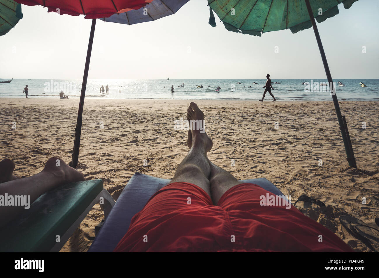 couple lying on beach chairs in front of indian ocean with blue sky and sun Stock Photo