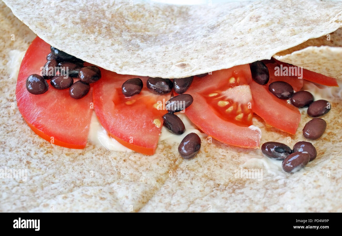 White flour tortilla with a bit of mayo, black beans and sliced tomato Stock Photo