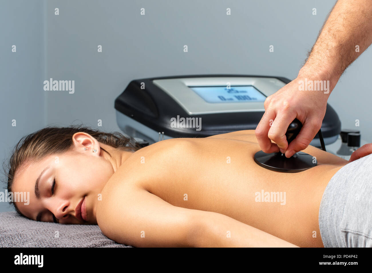 Close up of young woman having electrotherapy session.Therapist stimulating nerves and muscles on female spine. Stock Photo