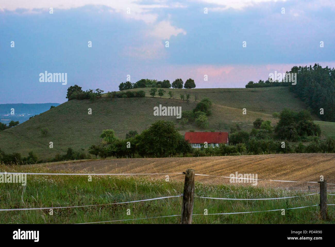Landscape with a single German house surrounded by trees, hills, blooming meadows and agricultural fields, at blue hour near Michelbach town, Germany. Stock Photo