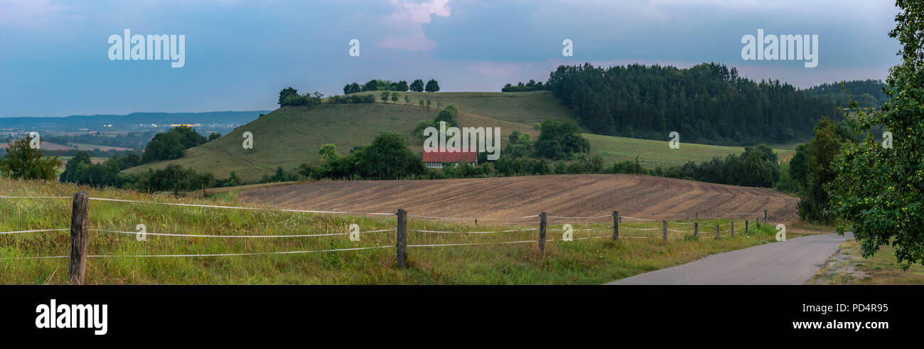 Blue hour countryside landscape with forest, hills and agricultural fields, country road and a house, on a summer day, near Michelbach town, Germany. Stock Photo