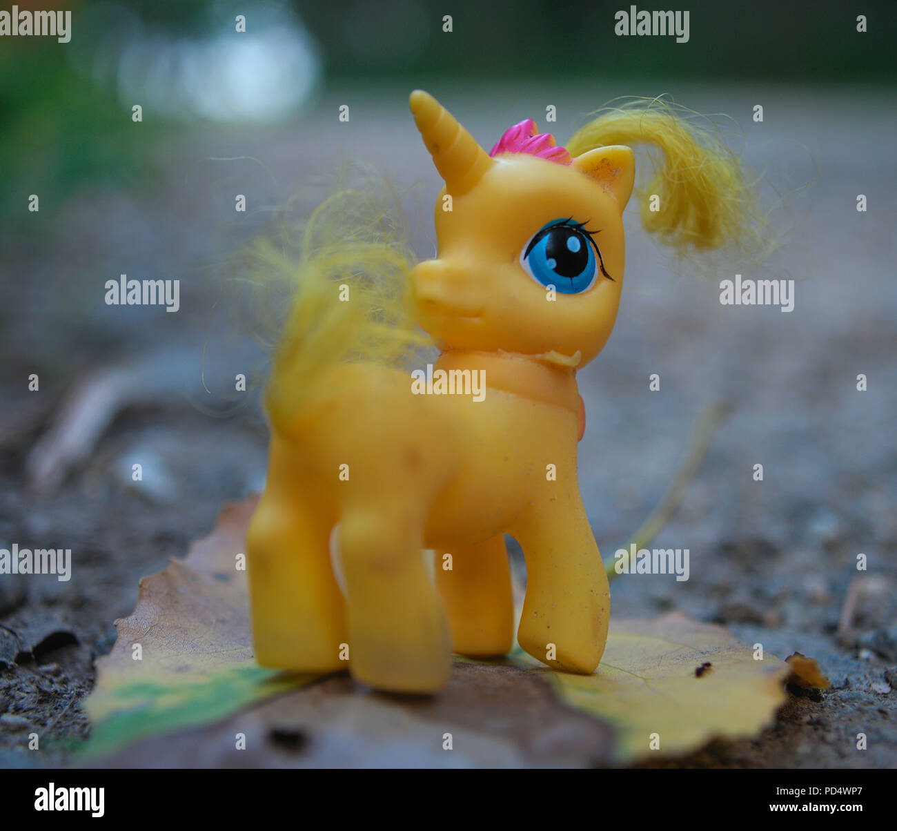 Yellow toy unicorn standing on leaf at forest road Stock Photo