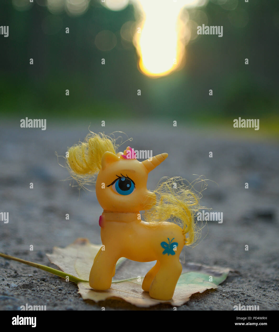 Yellow toy unicorn standing on leaf at forest road Stock Photo