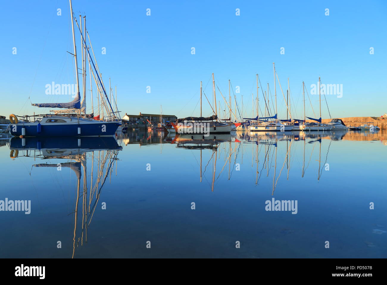 Sailing boats reflected on the water in Lyme Regis harbour known as The Cobb Stock Photo
