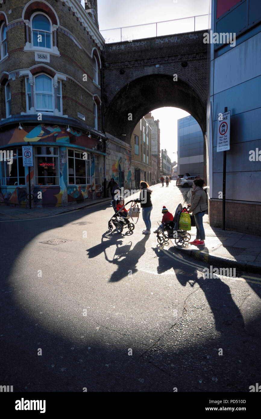 People walk on the sunny part of the street under railway bridge in Brixton, London Stock Photo
