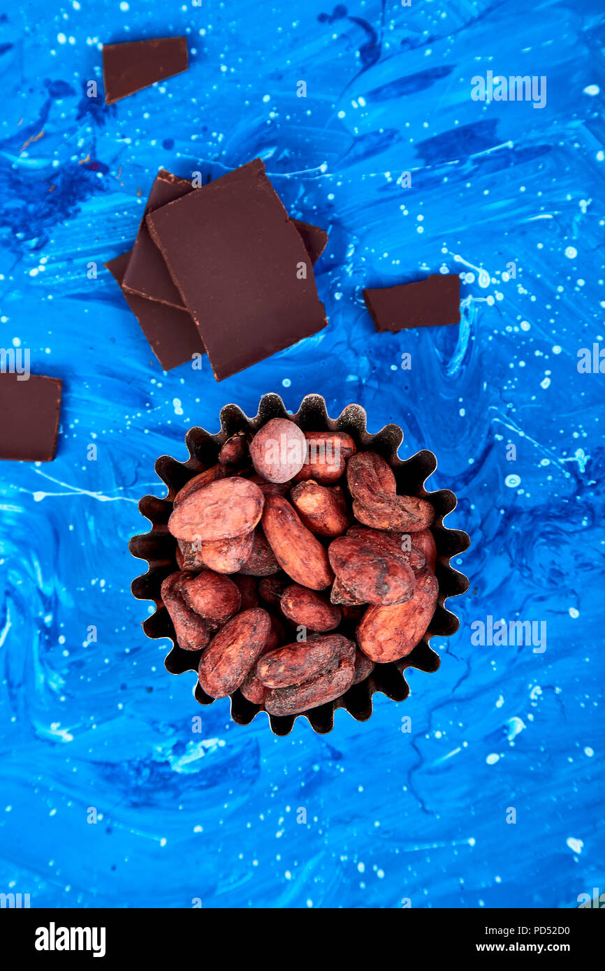 Cocoa beans background on blue table. Dark chocolate pieces and crushed cocoa powder carob. Top view. Copy space. Stock Photo