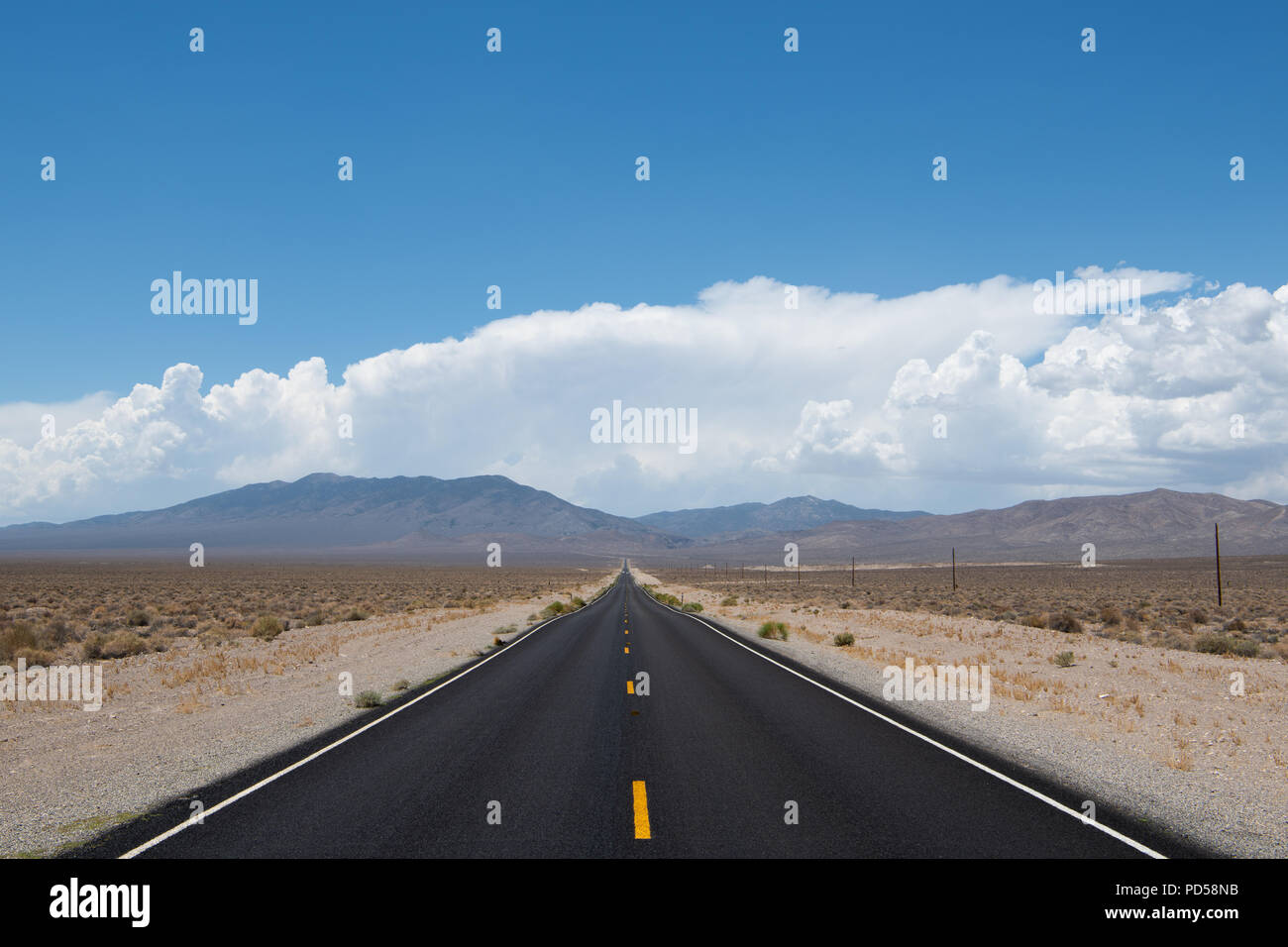 Desert highway vanishing into perspective into a mountain range under dramatic blue sky and white clouds in western Nevada Stock Photo