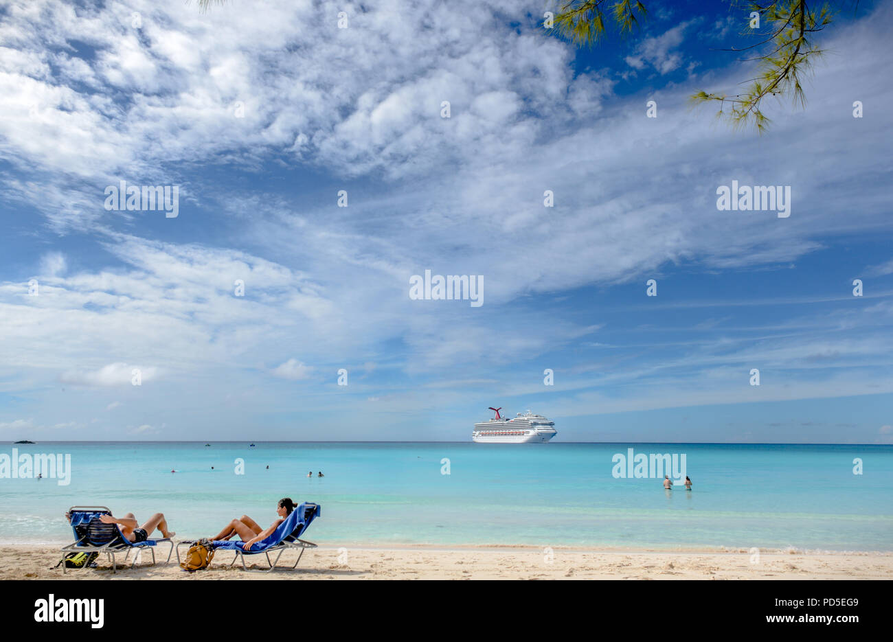 Couple relaxing in the beach chairs with ship on the back on Caribbean island of Half Moon Cay Stock Photo