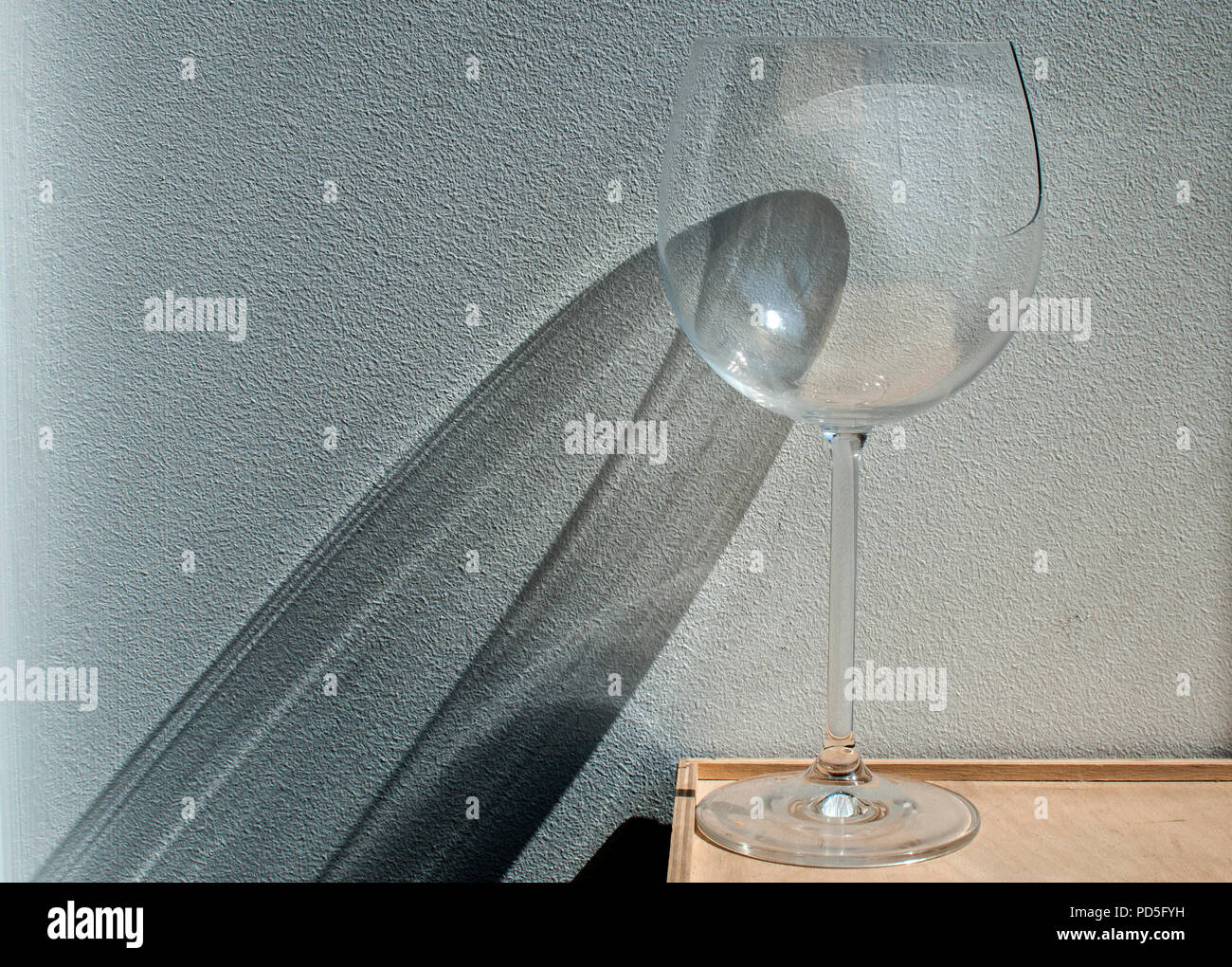 Broken wine glass with reflection from sunlight beam on wall plaster background Stock Photo