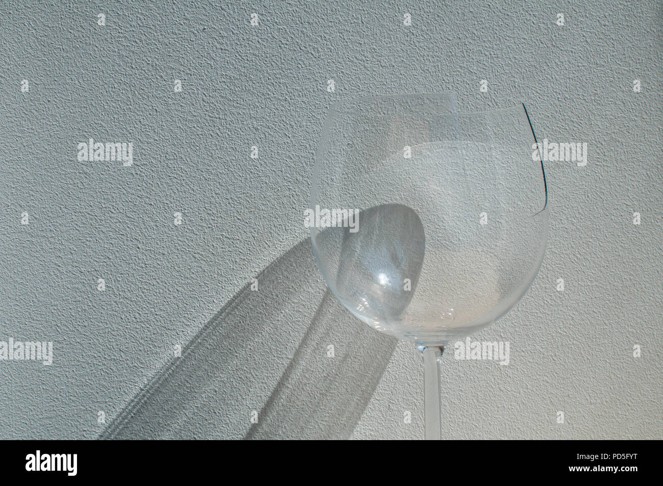 Broken wine glass with reflection from sunlight beam on wall plaster background Stock Photo