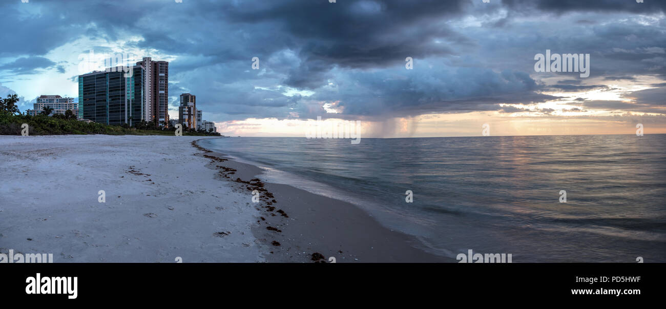 Rain pours from dark clouds over Clam Pass Beach in Naples, Florida around sunset. Stock Photo