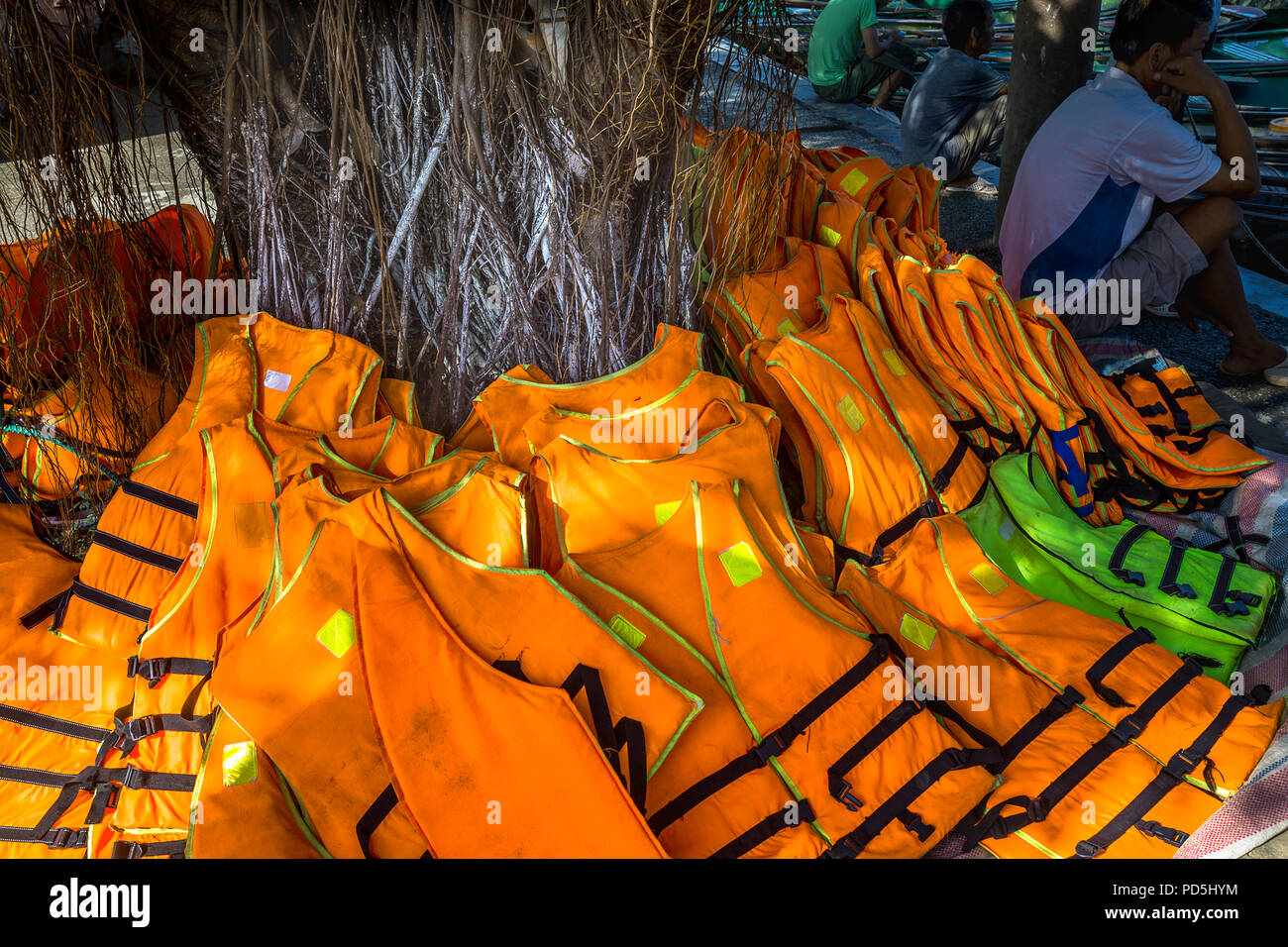 A group of orange lifejackets leaning against a tree at Tam Coc, Vietnam. Stock Photo