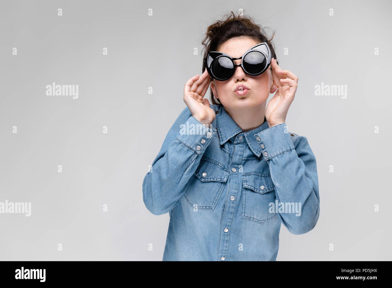 Young brunette girl in black glasses. Cat glasses. The hair is gathered in a bun. The girl adjusts her glasses. Stock Photo
