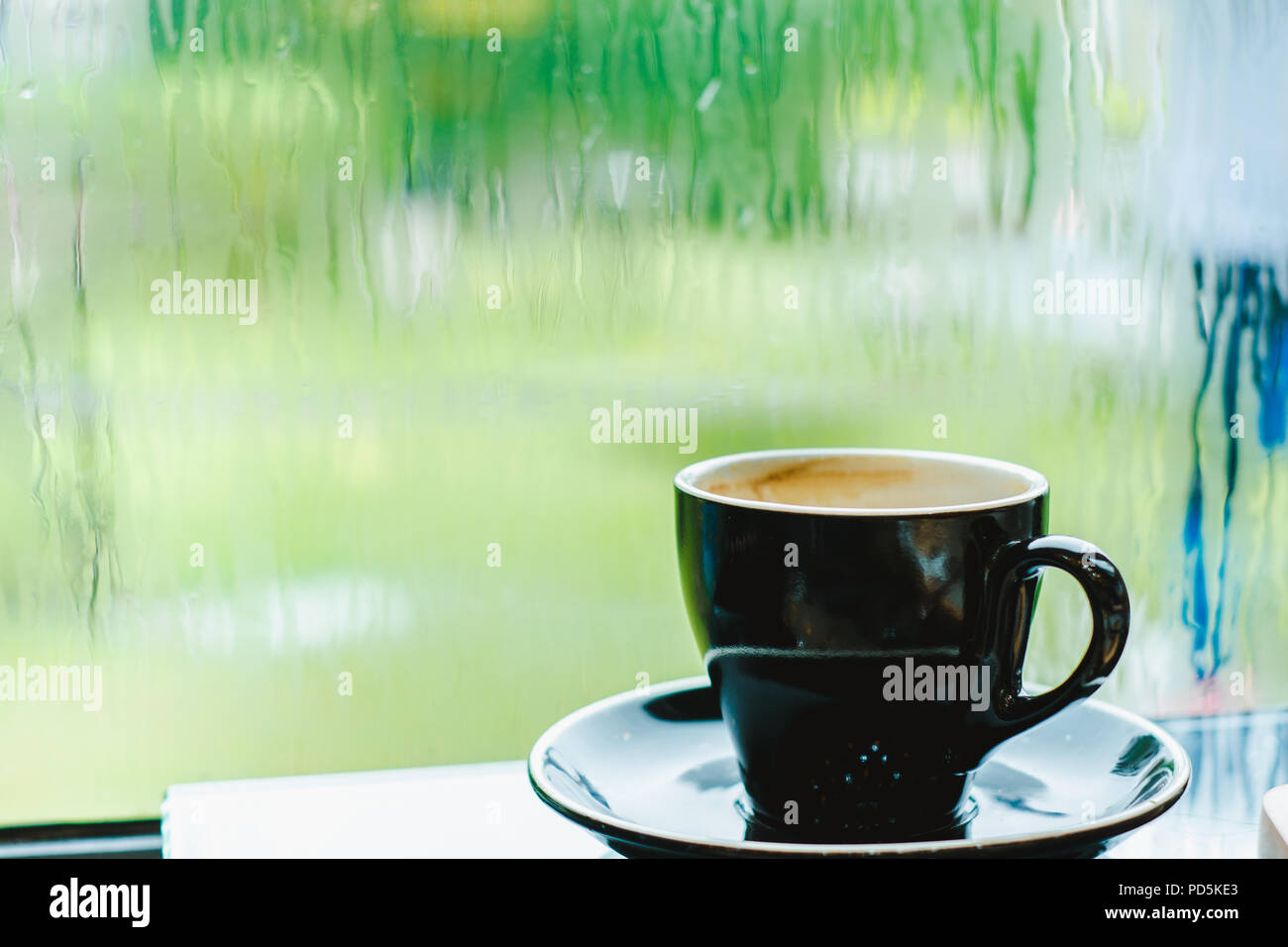 Black coffee cup on table in cafe restaurant near window in garden when raining in garden outside shop,Food and drink concept,Leisure lifestyle Stock Photo