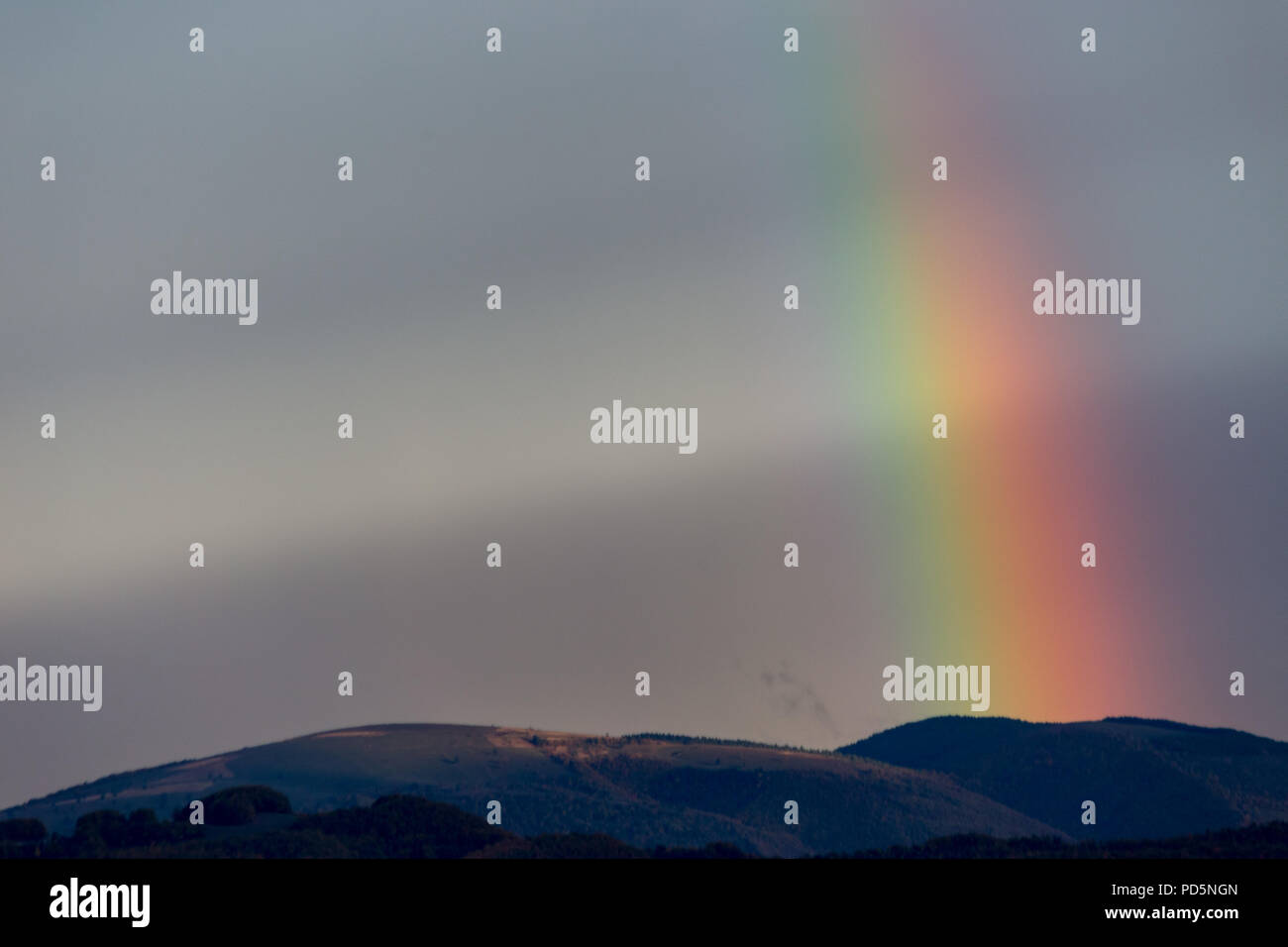 Beautiful and surreal view of part of a rainbow over some hills Stock Photo