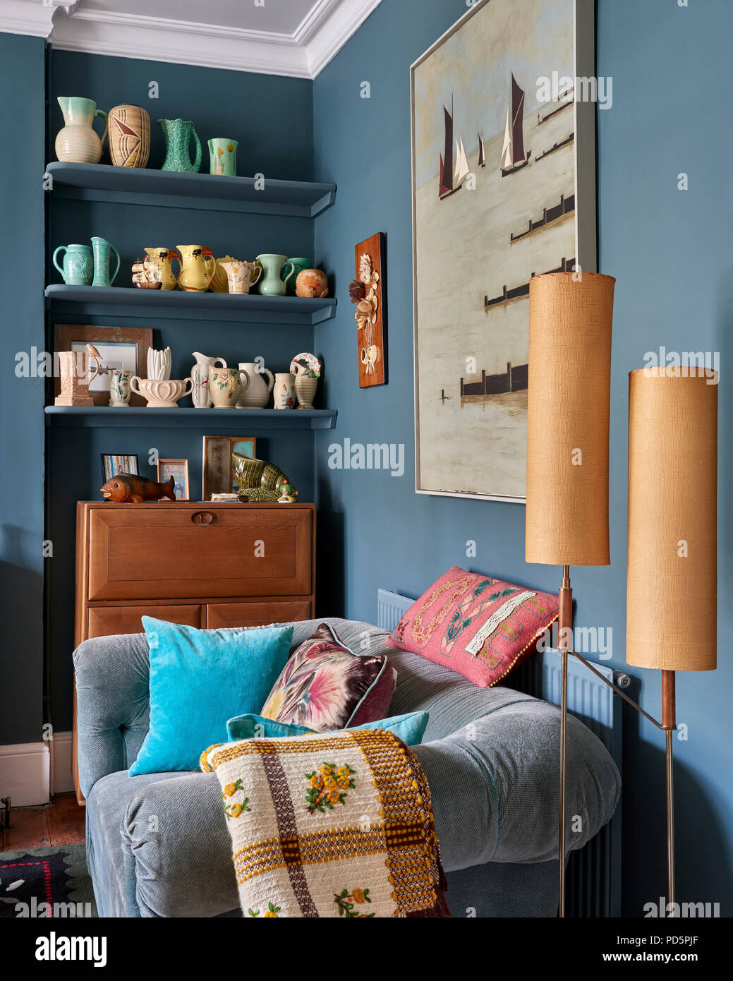 Colourful collection of vases and jugs displayed on custom made shelves in living painted in Farrow & Ball's Inchrya. the painting above the sofa is b Stock Photo