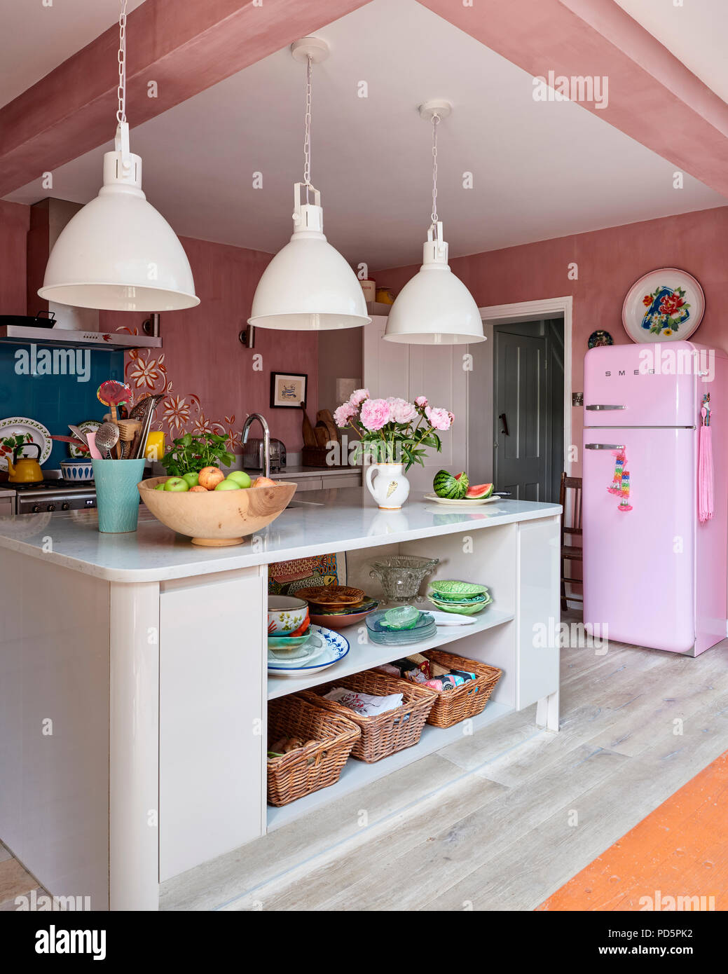 Large industrial style pendant lights and a pink Smeg fridge in light kitchen with walls painted in Authentico's Venetian Pink Chalk Stock Photo