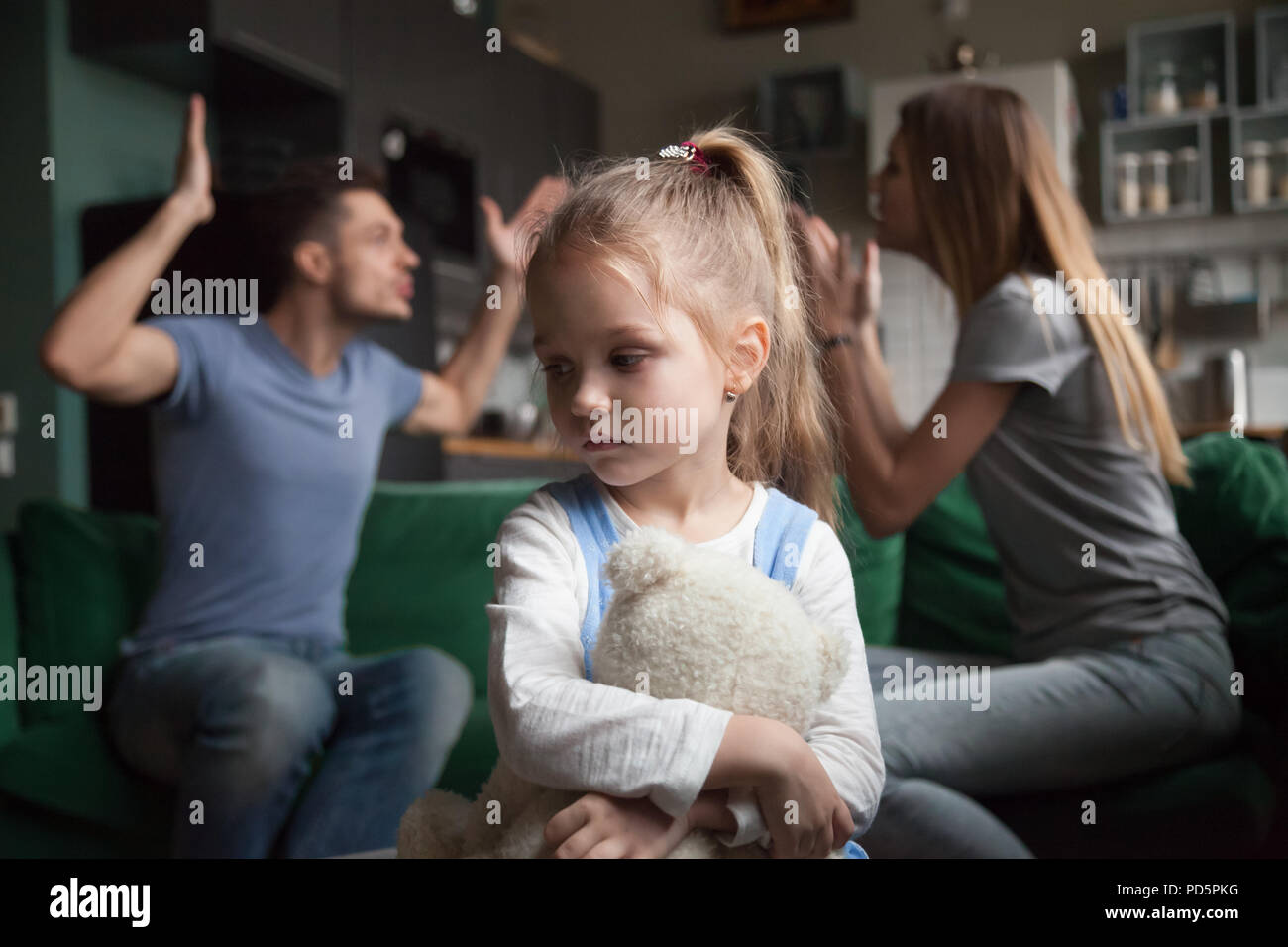 Kid daughter feeling upset while parents fighting at background Stock Photo