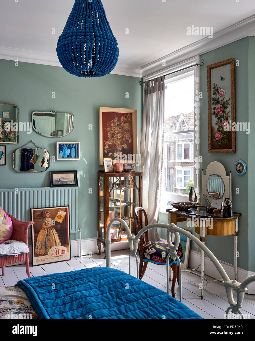 Vintage mirrors and artwork by Jo Oakely on wall in light bedroom painted in Little Greene's Cupboard Green. The blue bead chandelier is from Graham & Stock Photo