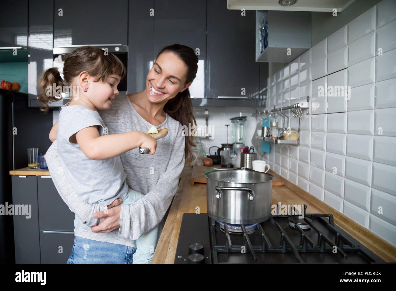 Smiling mom holding kid daughter curious about cooking in kitche Stock Photo
