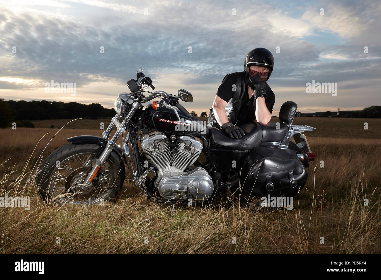 Leather clad biker posing for a photoshoot on his custom Harley Davidson XL883 Sportster Low cruiser motorcycle, on the Beverley westwood, East riding Stock Photo
