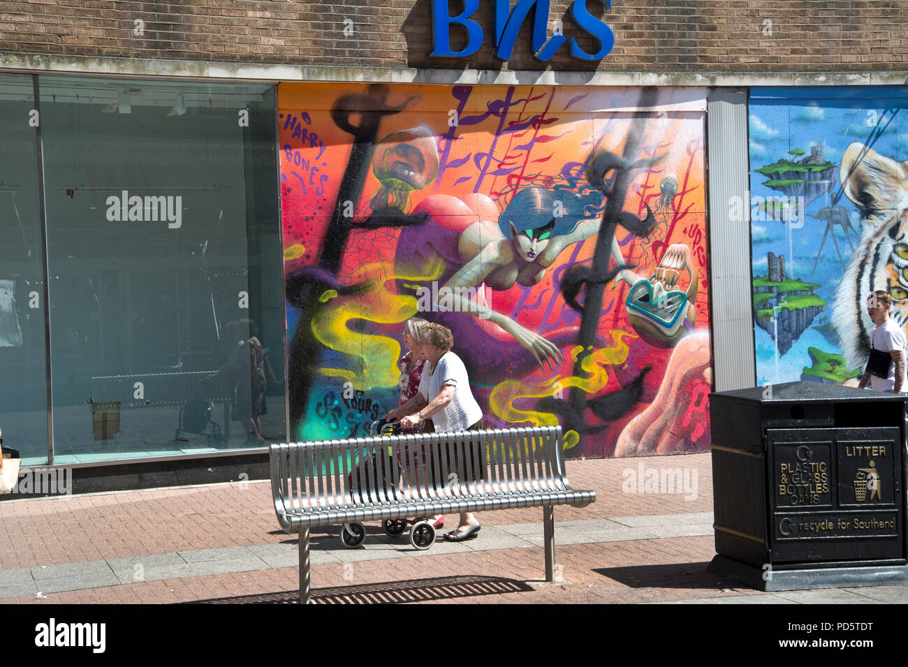 Southend on Sea, Essex. Two older women walk past a closed down BHS (British Home Stores) shop now decorated with colorful street art Stock Photo