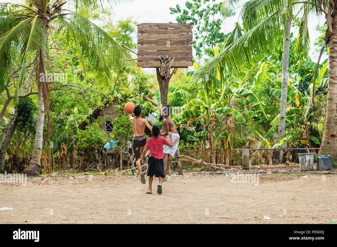 Sandugan, Siquijor, Philippines - May 13 2013: Three kids playing basketball at sand field with old wooden basketball basket Stock Photo