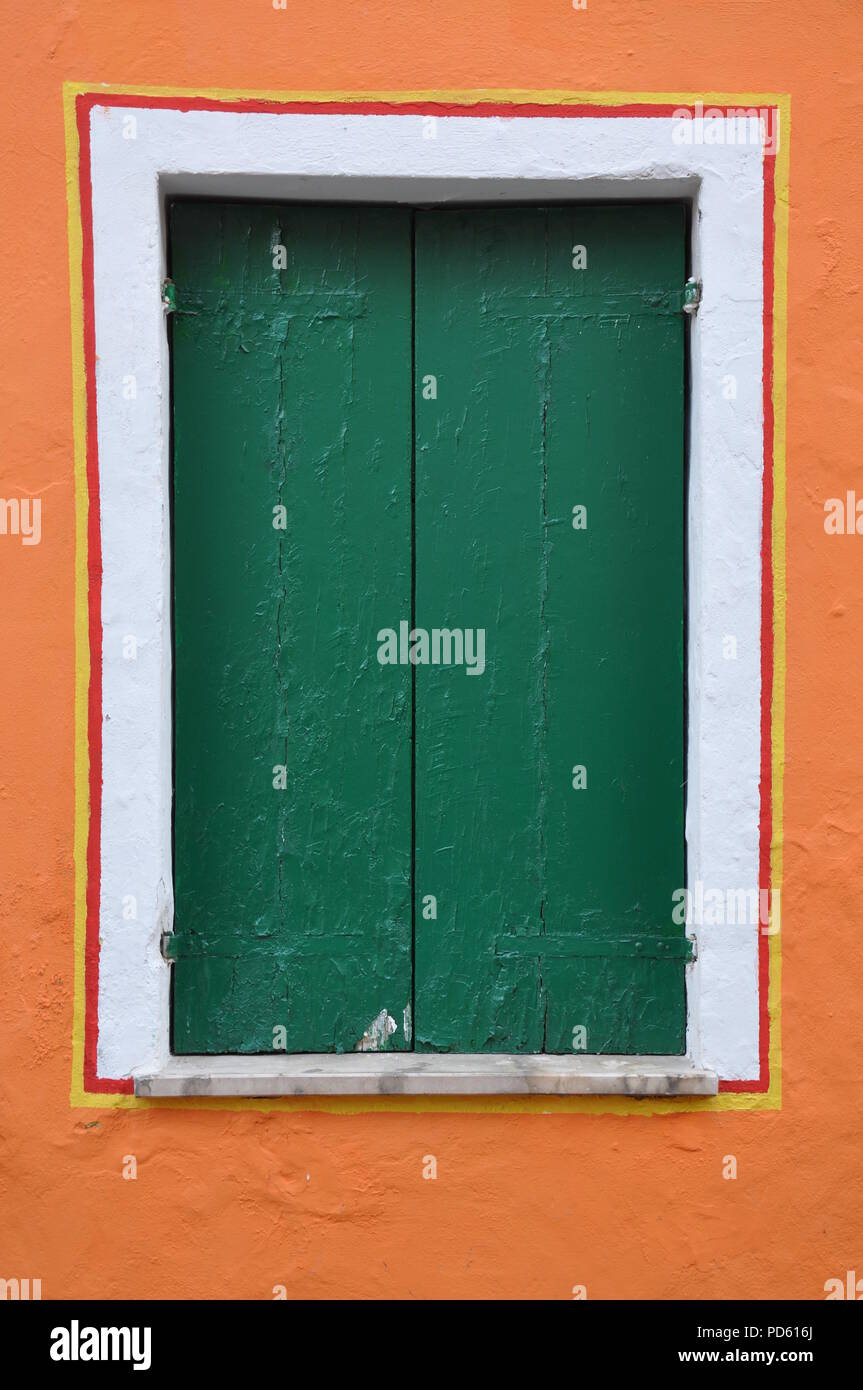 Closed window with green shutter on orange wall Stock Photo