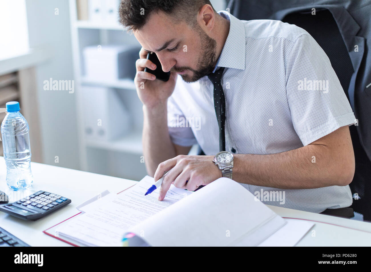 A man is sitting in the office, working with documents and talking on the phone. Stock Photo