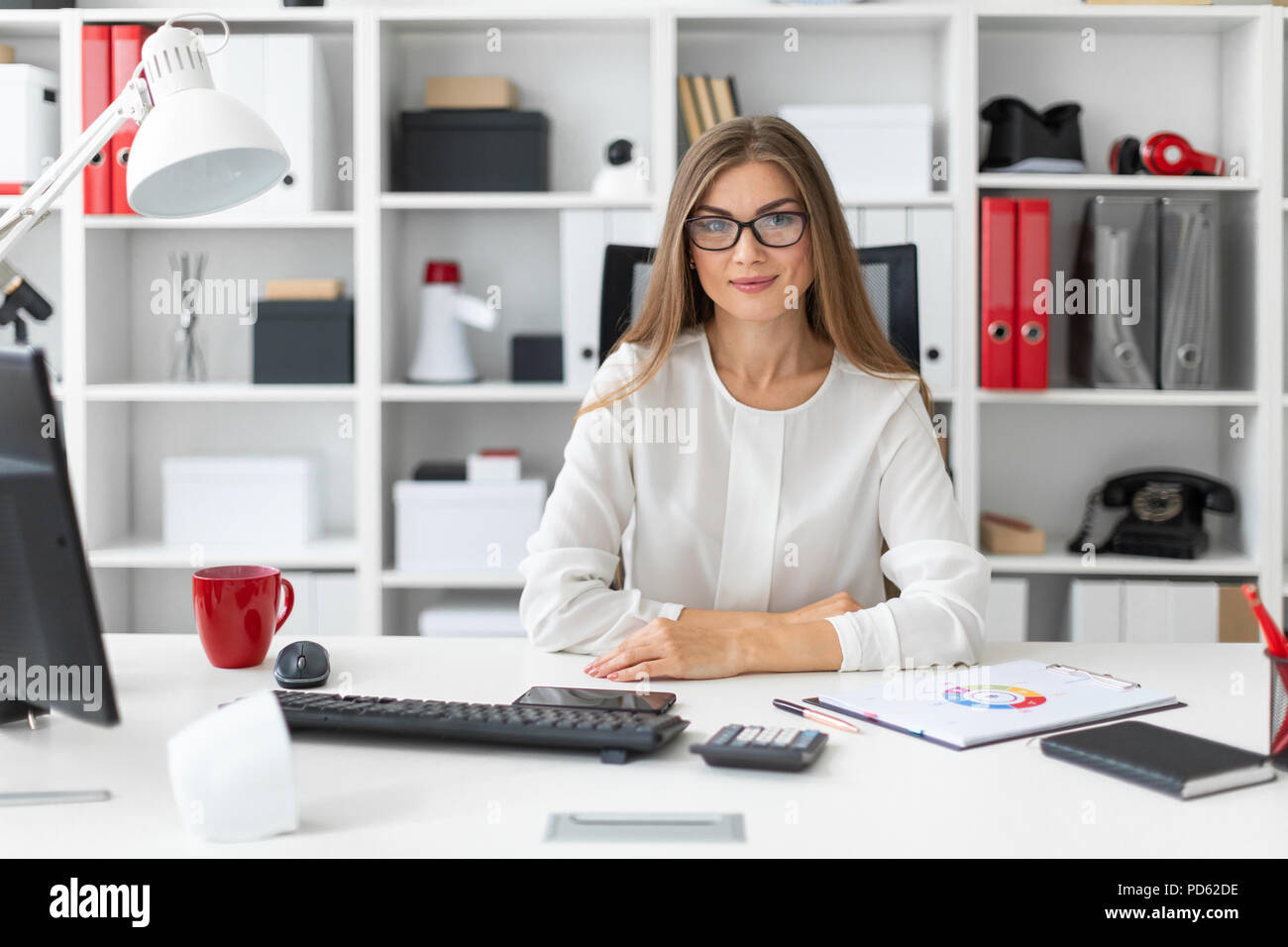 A young girl is sitting at the computer desk in the office. Stock Photo