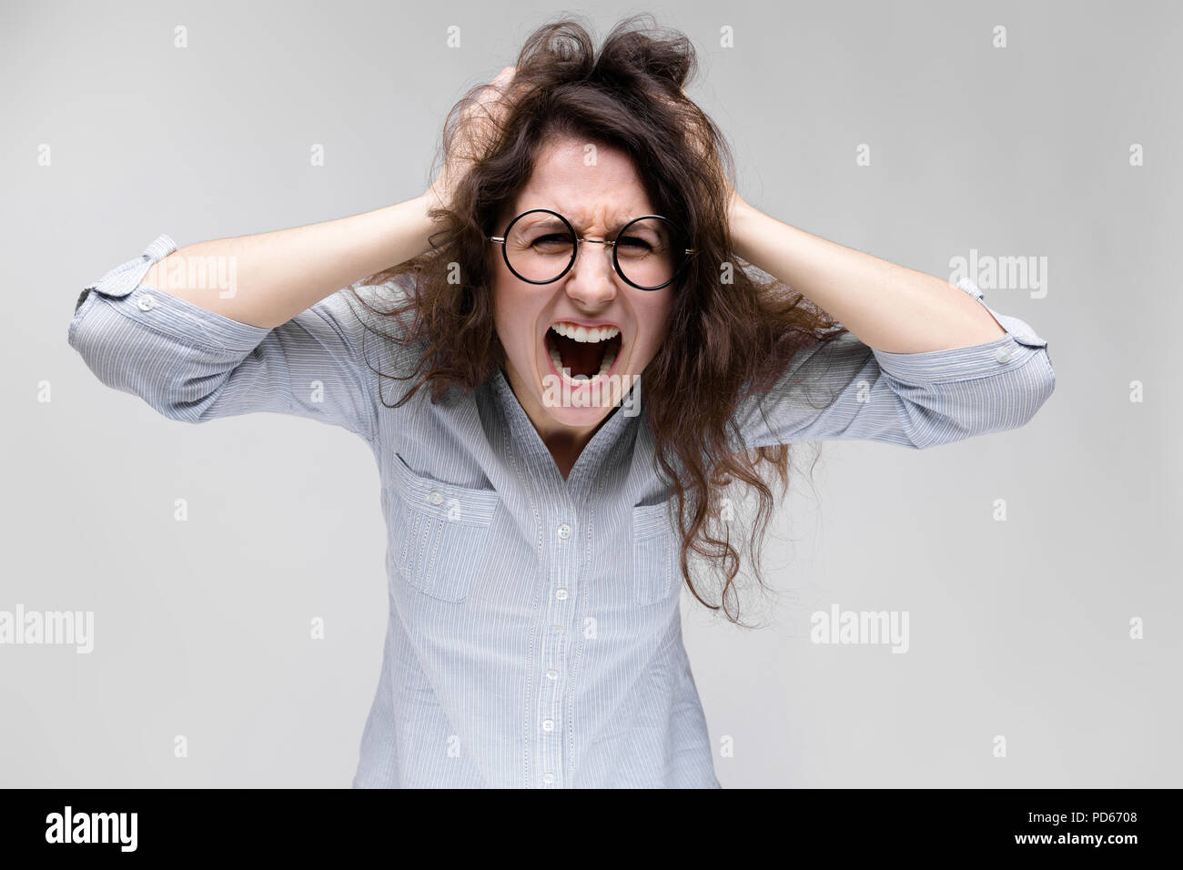 Young brunette girl with glasses. The girl grabbed her head and shouted. Stock Photo