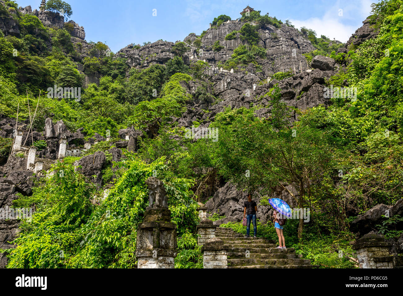 A man and woman with an umbrella on the stone stairway up from Mau Cave, Tam coc, Vietnam Stock Photo