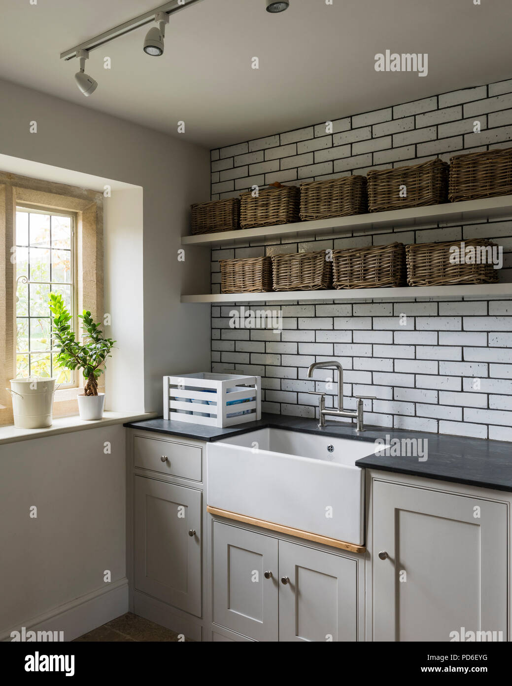 Wicker baskets on shelving above Butler sink in tiled utility room. Stock Photo
