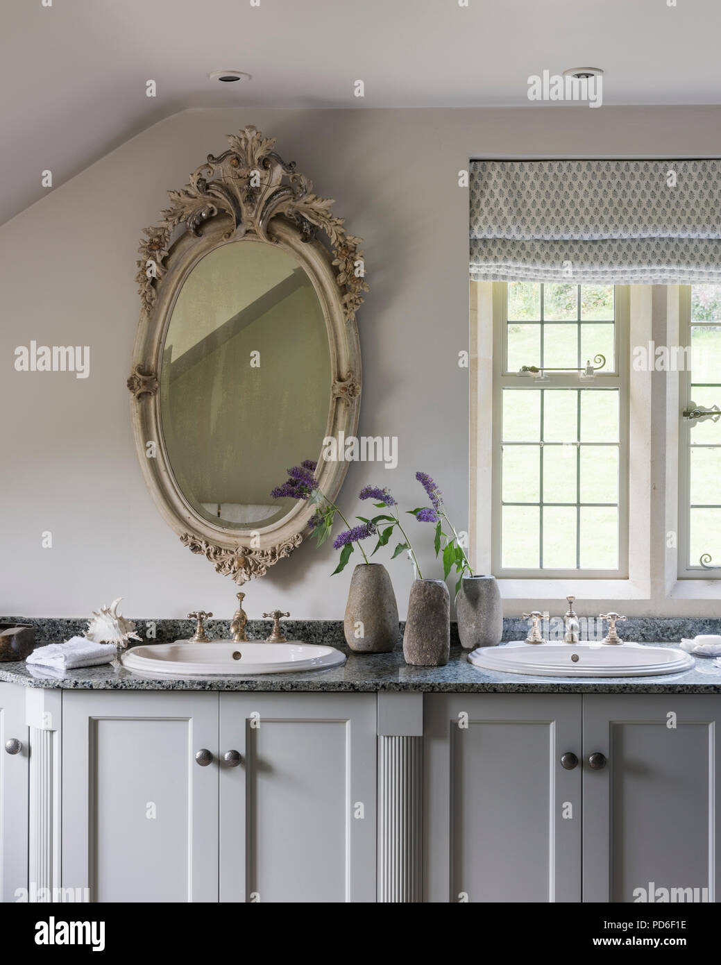 Decorative antique mirror above washbasin with single stem flowers in stoneware vases. Stock Photo
