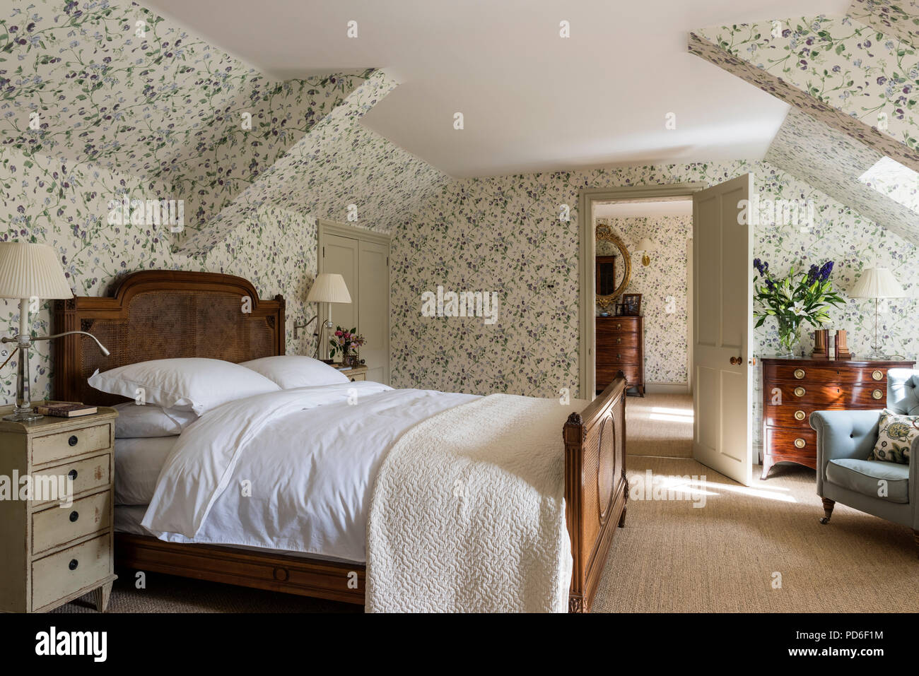 Antique wicker bed in floral papered bedroom with white lamps and wuilt Stock Photo