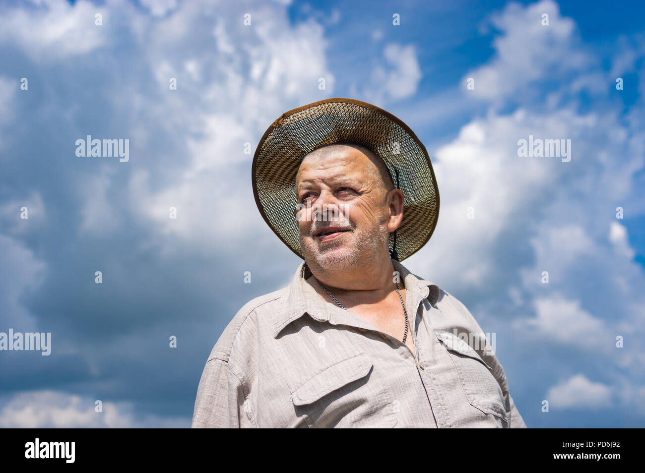 Nice portrait of Ukrainian senior farmer in straw hat against blue cloudy sky Stock Photo