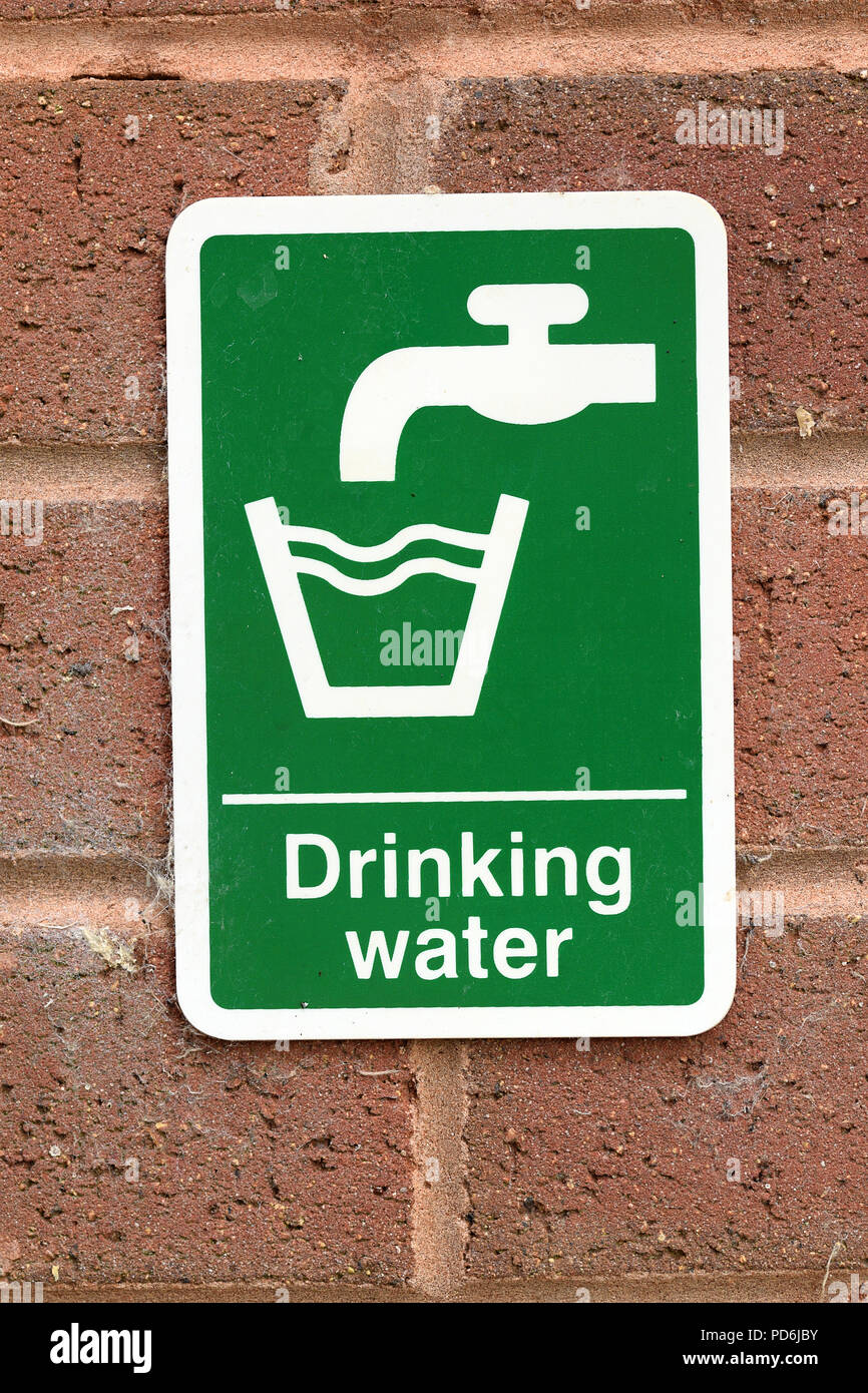 Drinking water sign with white text and tap faucet symbol and glass symbol on green background on red brick wall. Environmental water issues concept Stock Photo