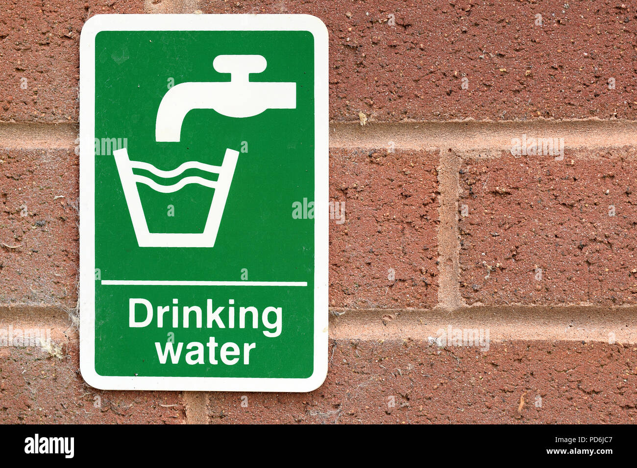 Drinking water sign with white text and tap faucet symbol and glass symbol on green background on red brick wall. Environmental water issues concept Stock Photo