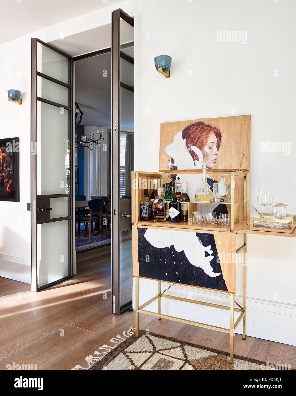 Drinks cabinet with artwork at double height doorway with blue and gold wall lights Stock Photo