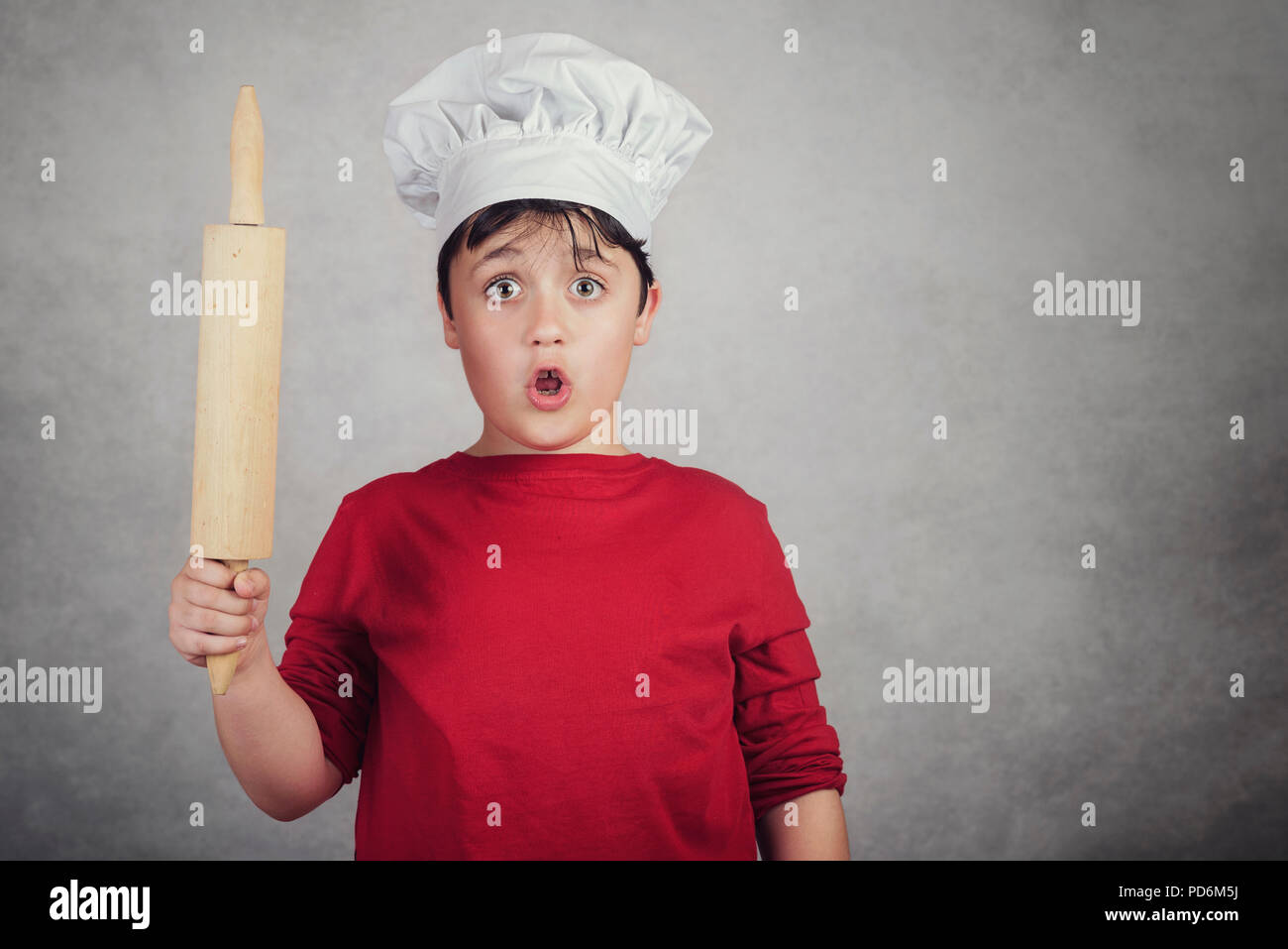 child cook surprised with a rolling pin on gray background Stock Photo