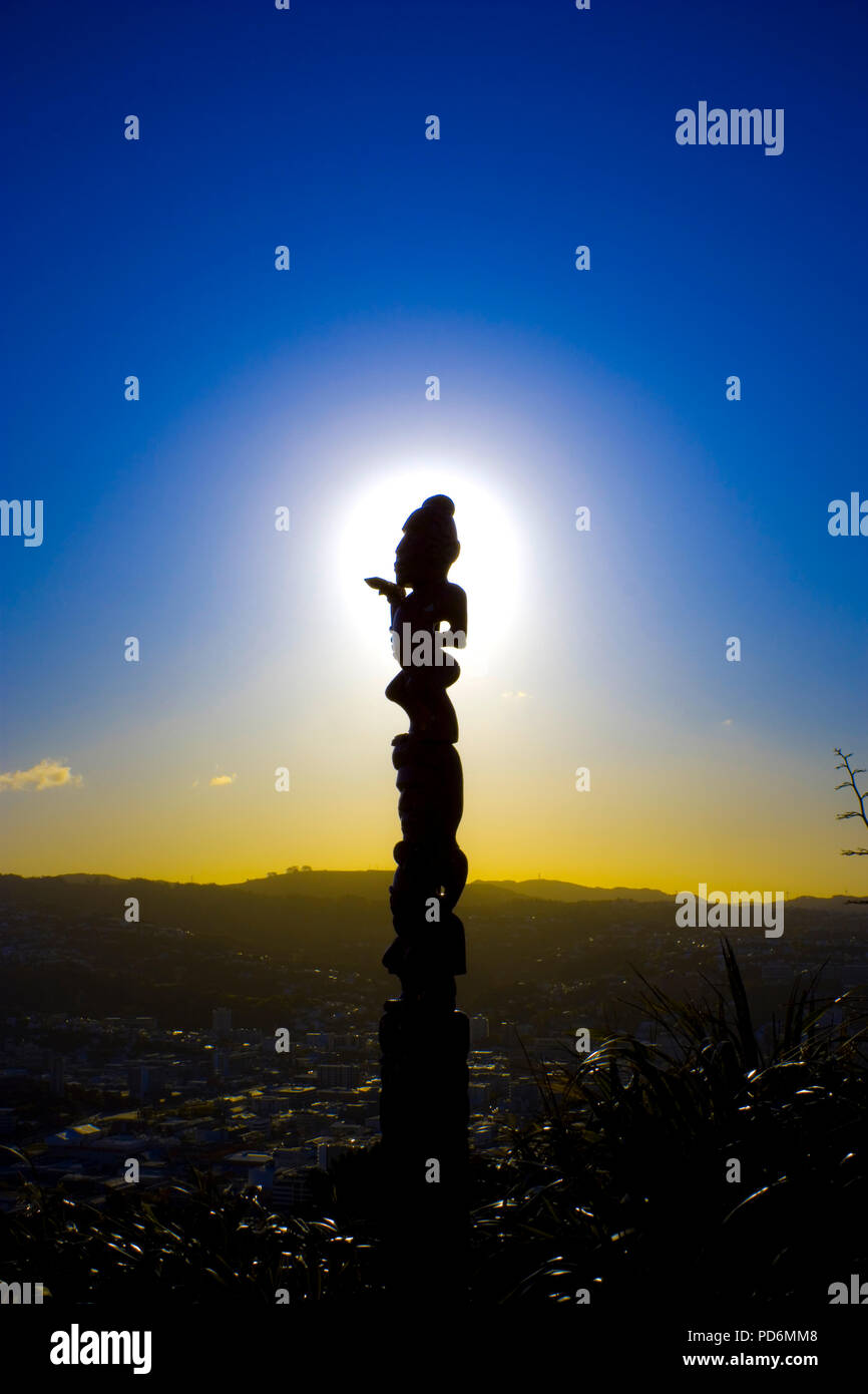 Maori art hand carved statue in Wellington with view over the city scape during sunset blue hour representive for the New Zealand native culture Stock Photo