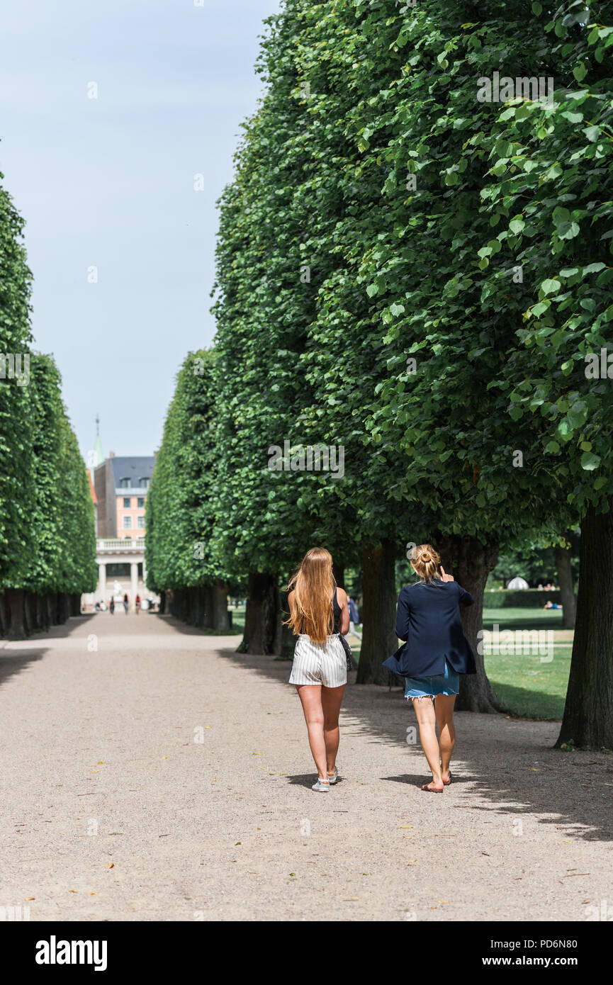 Young women relaxing during a summer day in a Danish park, perfectly manicured linden trees line an elegant garden alley. Concept of hygge. Stock Photo