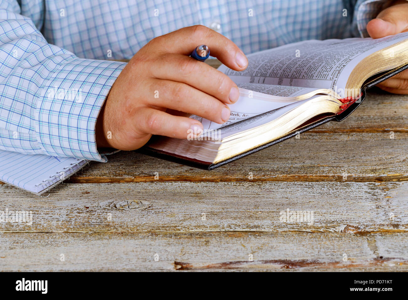 Man is holding a pen in his hand with an open book Holy Bible lying in fornt of him Stock Photo