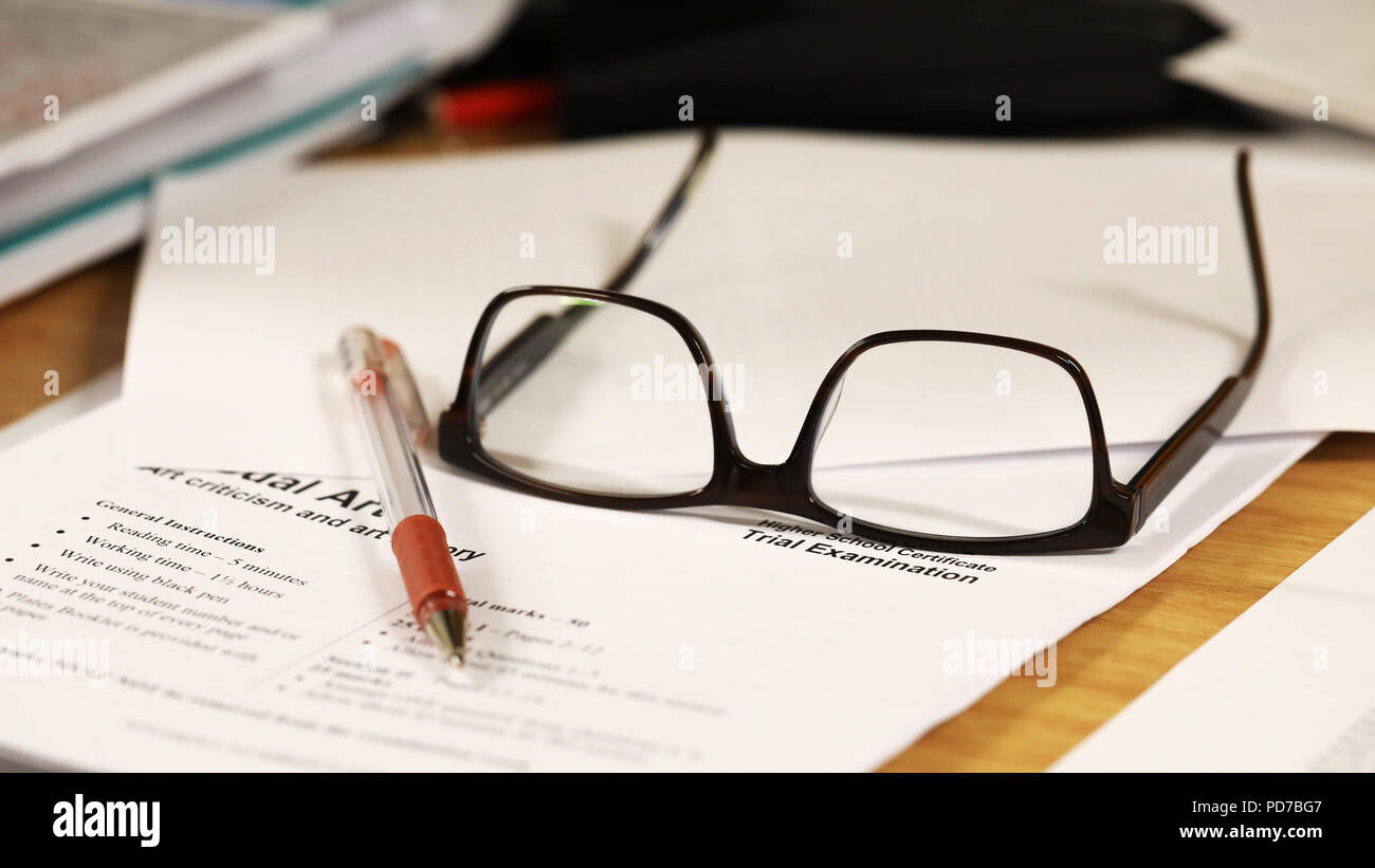 a school teachers desk with glasses and exam paper being marked on it. education, educator, teaching concept. Stock Photo