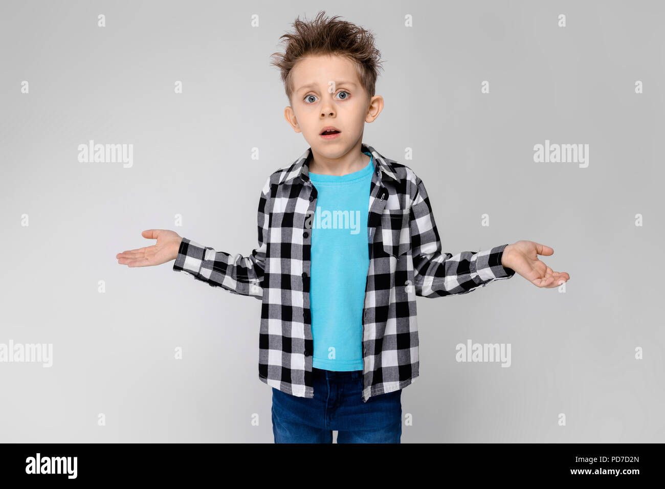 A handsome boy in a plaid shirt, blue shirt and jeans stands on a gray ...