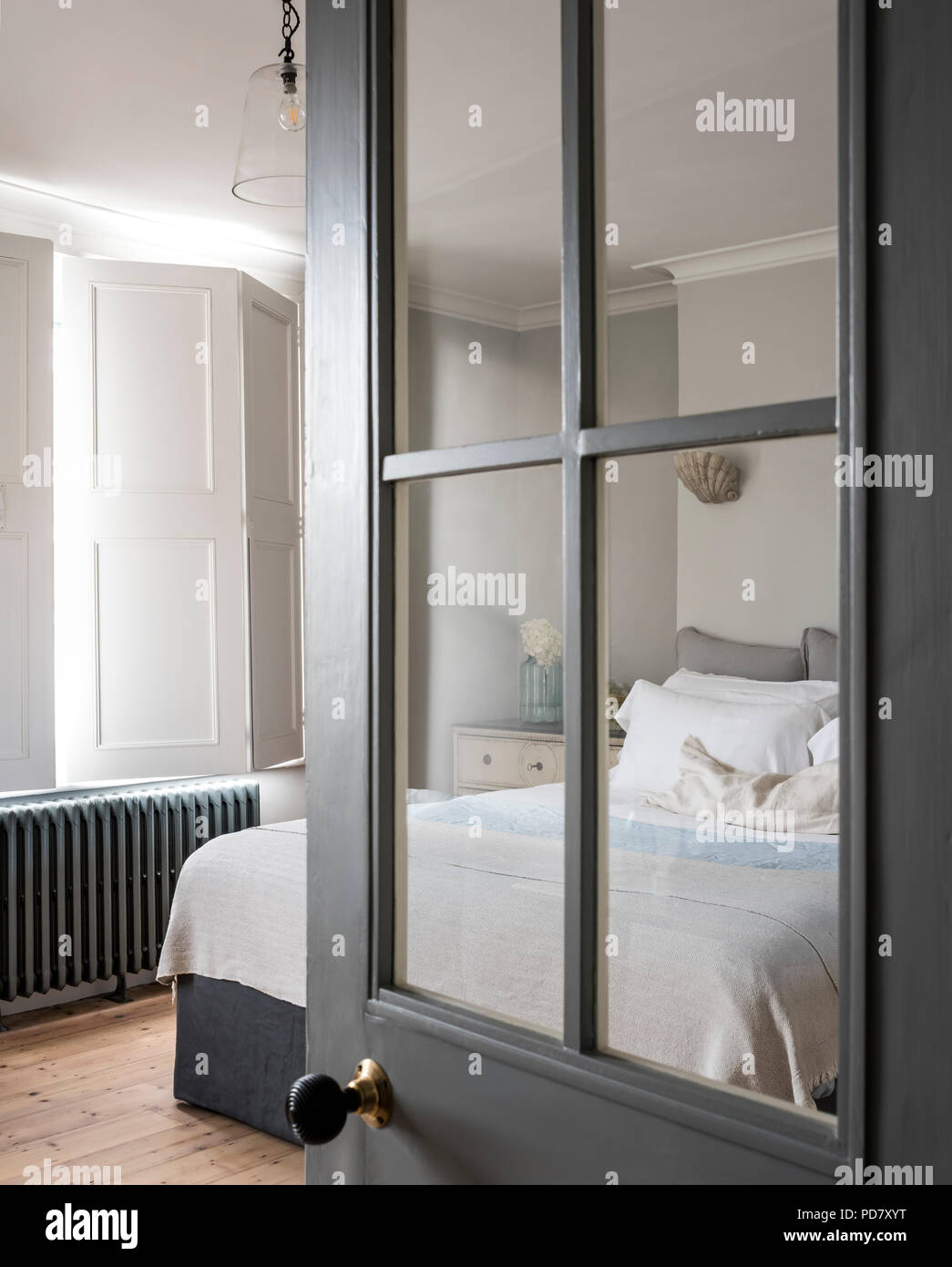 View through glass panelled door into elegant bedroom with window shutters and iron radiator Stock Photo