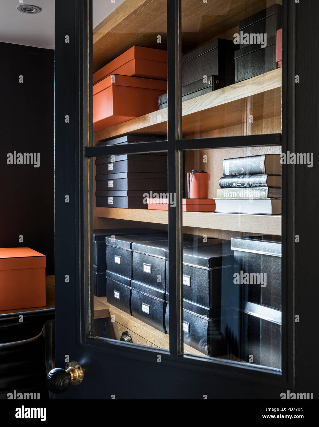 View through glass panelled black door into storage room with chic black and orange boxes Stock Photo